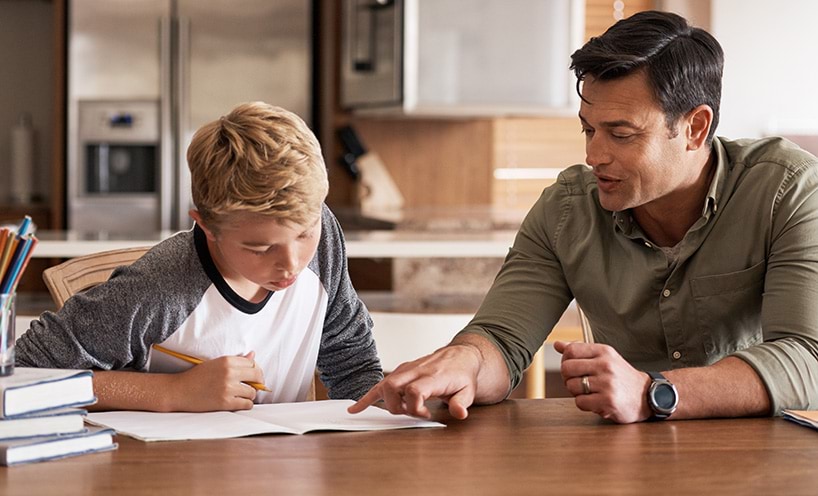 A father and son sit at a kitchen table working on a lesson 