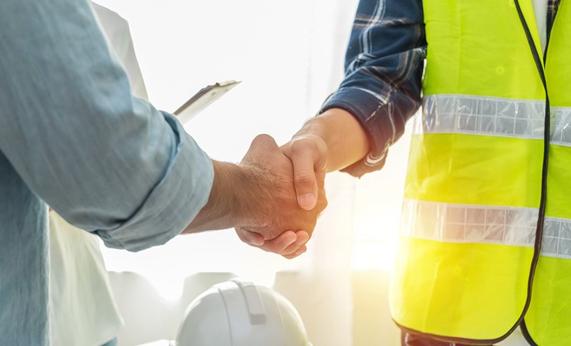 A person in a blue shirt and a person in a hi-vis vest shaking hands come to an agreeement