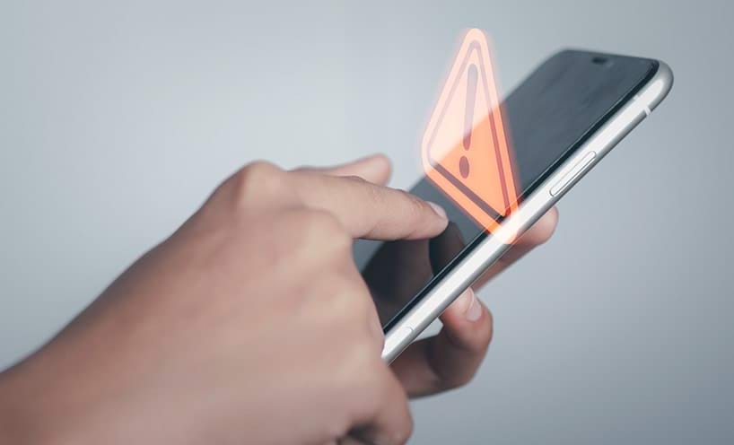 a human hand uses a mobile phone a warning symbol pops up