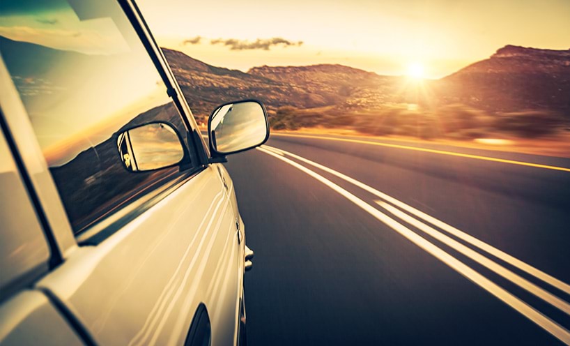 A view of  the side of a car, including a rear vision mirror, as it drives along an empty road