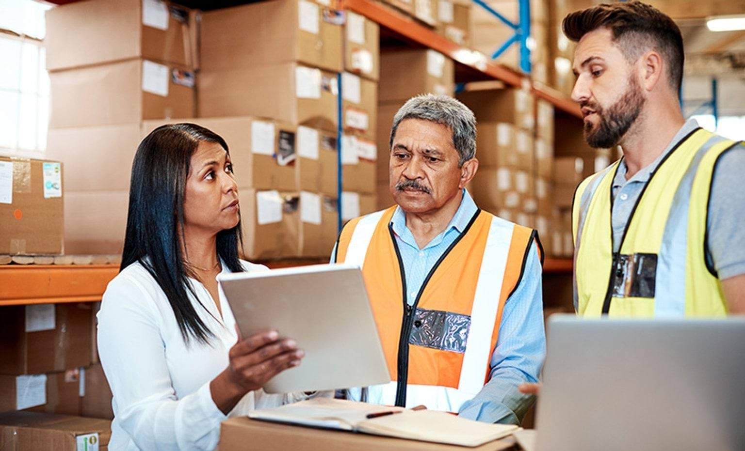 A warehouse with a woman and two men, the woman is holding up a paper