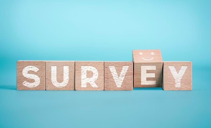 The word "survey" spelled out on wooden cubes, with the letter "e" slightly turned to show a smiley face on top of the cube.