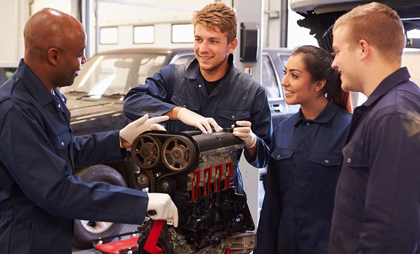 Teacher helping apprentices training to be car mechanics