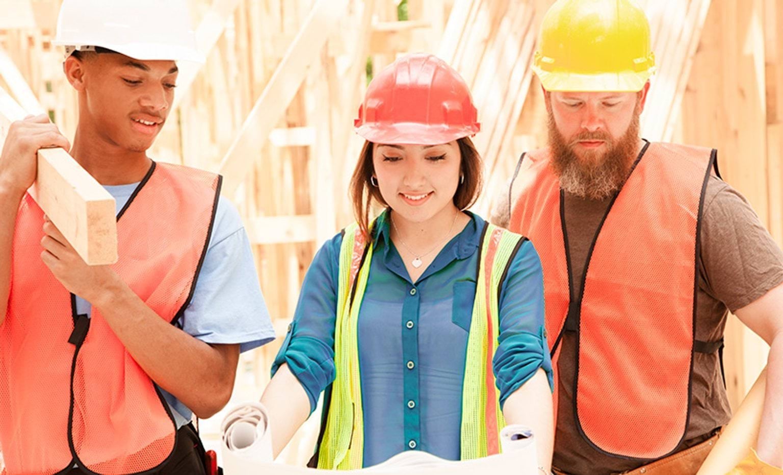 Construction workers wearing safety vests and hard hats looking at a plan inside an unfinished house.