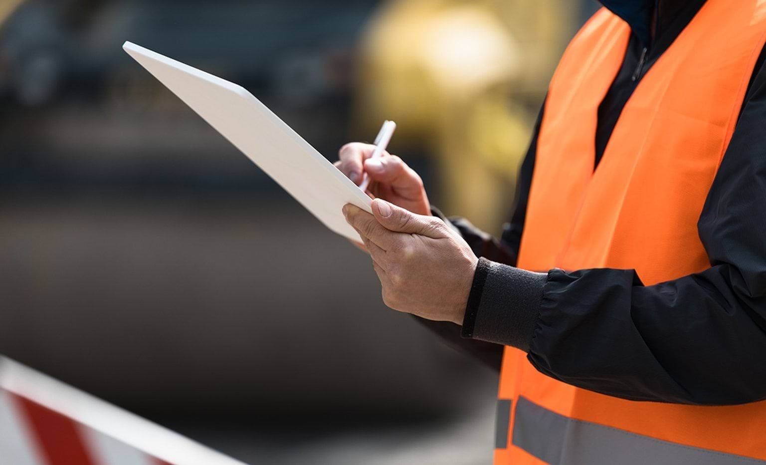 Construction site supervisor taking notes while wearing safety gear and overseeing project progress during daylight hours