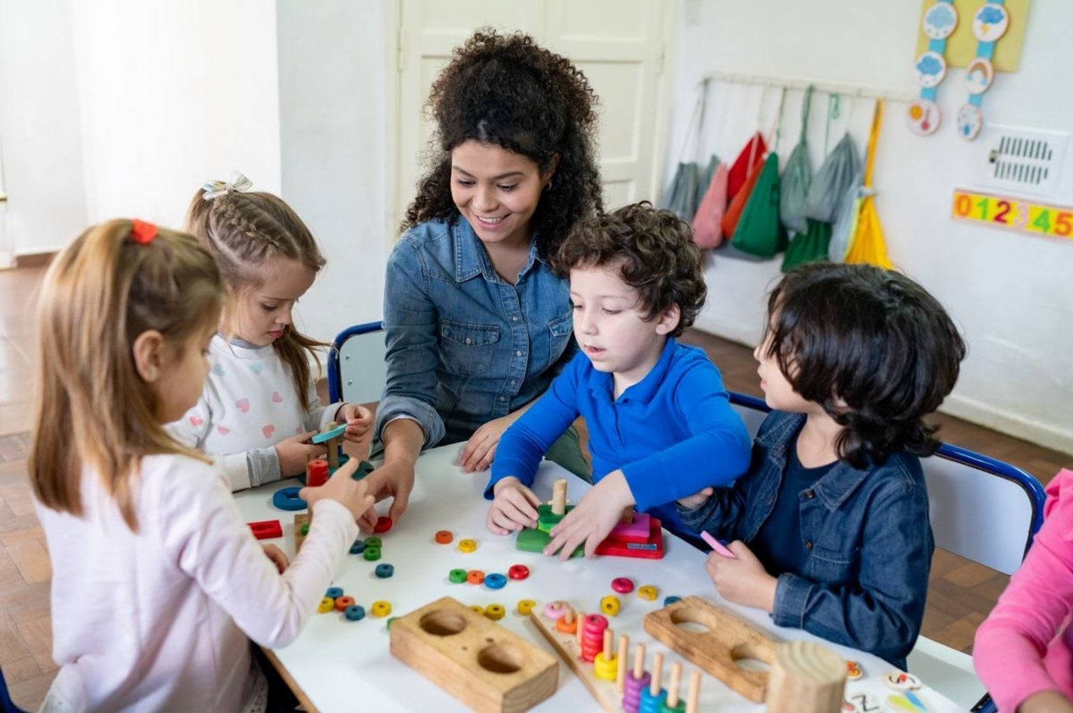 Group of young children playing with wooden toys with a young teacher