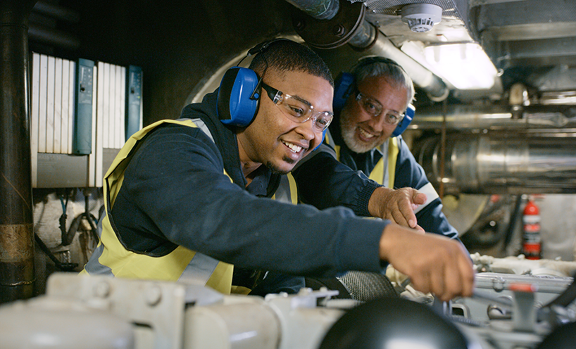Senior expert mechanic coaching a trainee in a manufacturing plant.