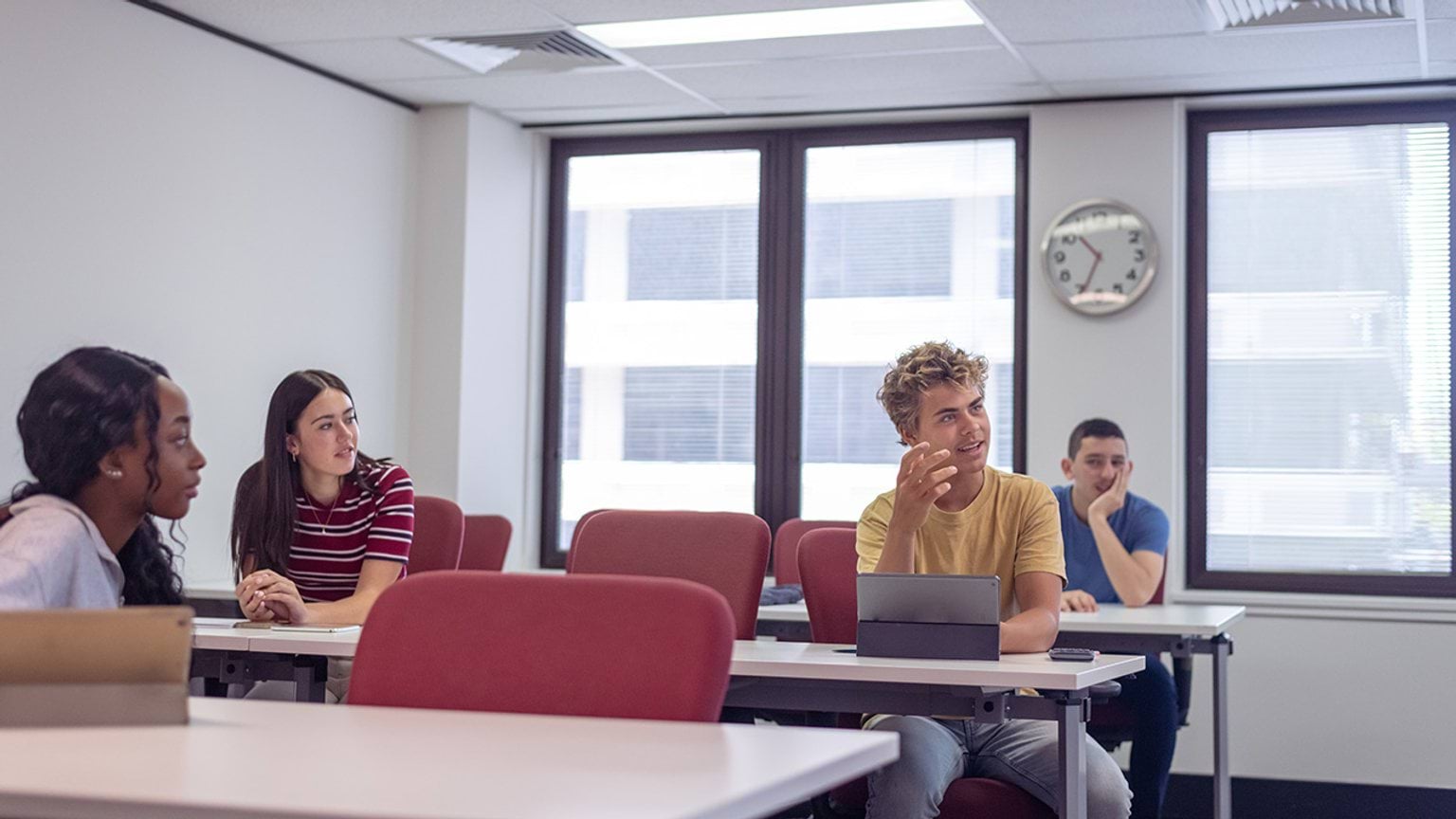 A group of students in high school sit at desks and listen as their teacher gives a lecture in class.